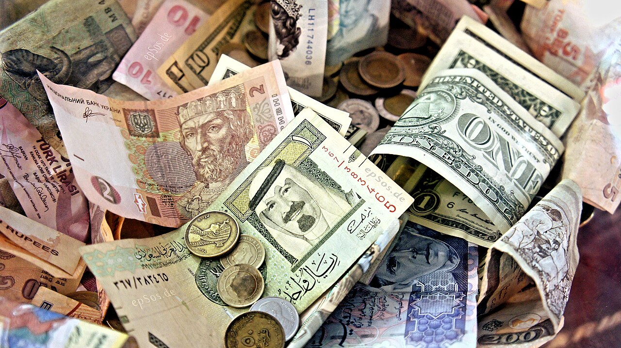 Persona revisando su teléfono para recibir dinero, con billetes de pesos sobre la mesa