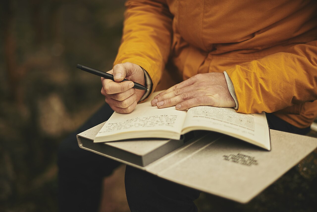 Person writing in a notebook next to their smartphone
